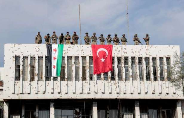 Turkey-backed Syrian rebel fighters and Turkish soldiers are seen on top of a building in the border town of Ras al Ain